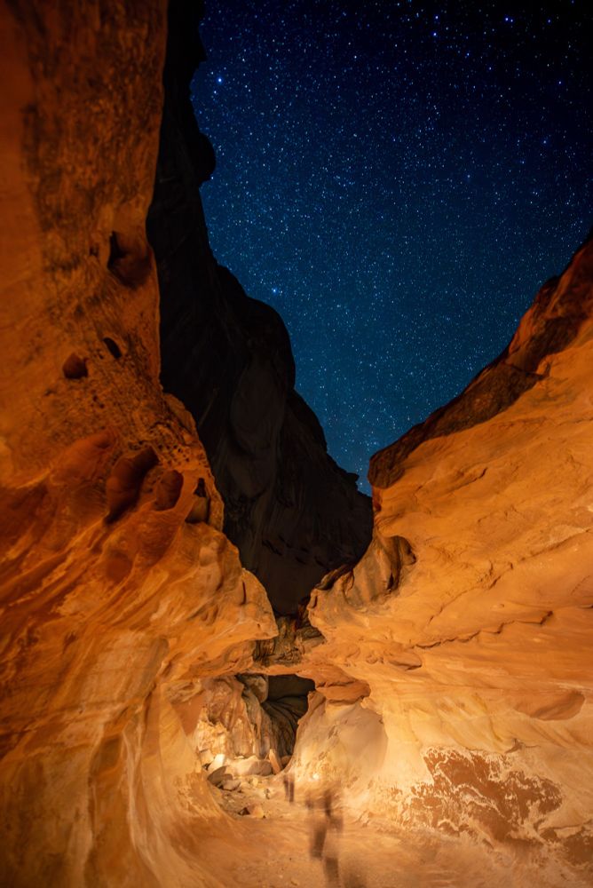 A sandstone slot canyon with overlapping rock features, with a narrow slit above showing a starry sky. 