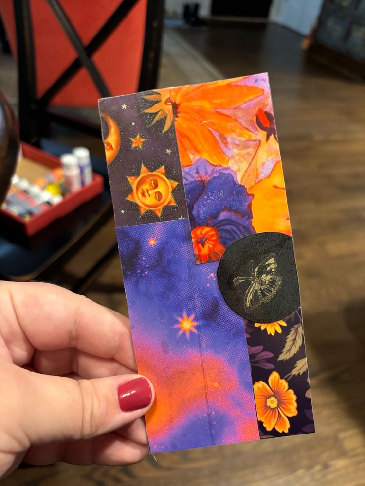 A handmade bookmark, featuring many scraps of different purple and orange patterned papers, as well as a golden ink butterfly stamp. 