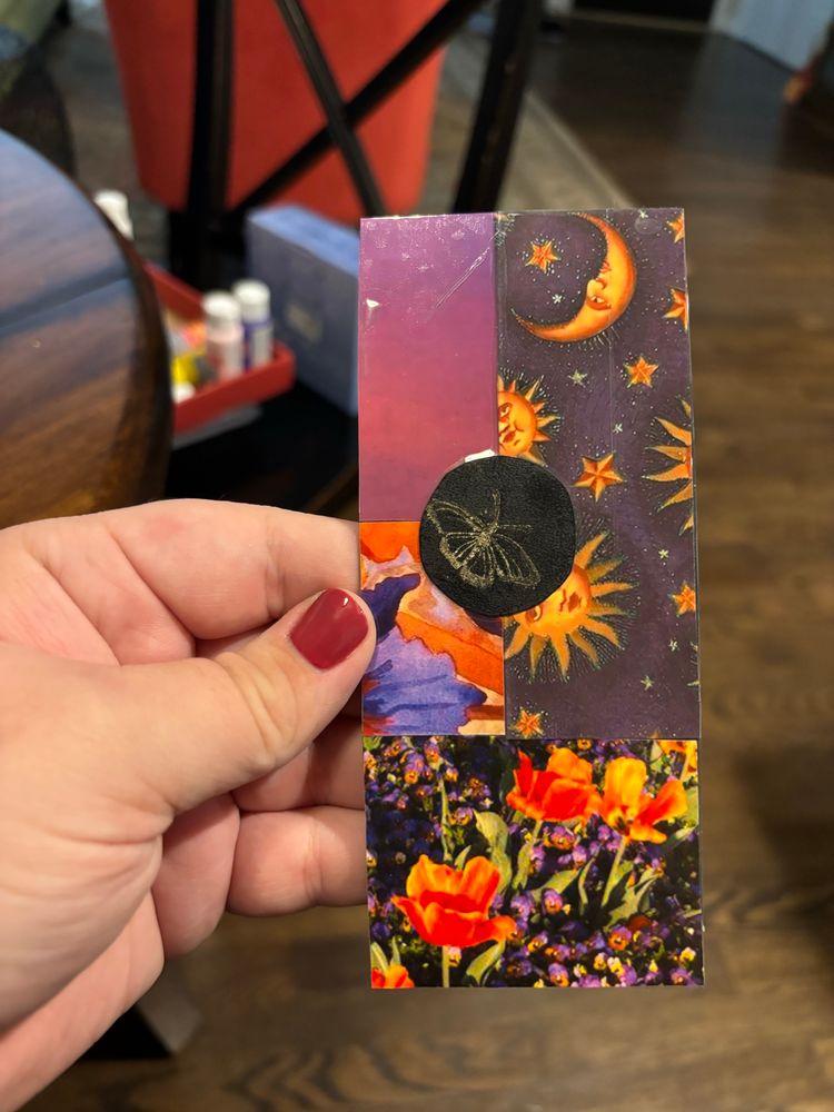 A handmade bookmark, featuring many scraps of different purple and orange patterned papers, as well as a golden ink butterfly stamp. 
