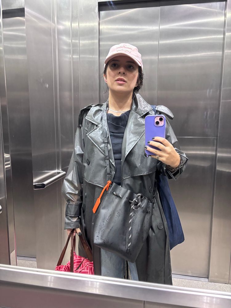 Eu num elevador fotografei a mim mesma no espelho. Visto uma capa de chuva preta que cobre todo o meu corpo. Embaixo blusa preta e bolsa da mesma cor pende cruzada ao corpo. Na mão direita seguro minha lancheira de marmita e na direita o celular que faz a foto. Estou de cabelo (castanho) preso num coque displicente e uso um boné rosa desbotado com os dizeres CUTE BUT PSYCHO. 
