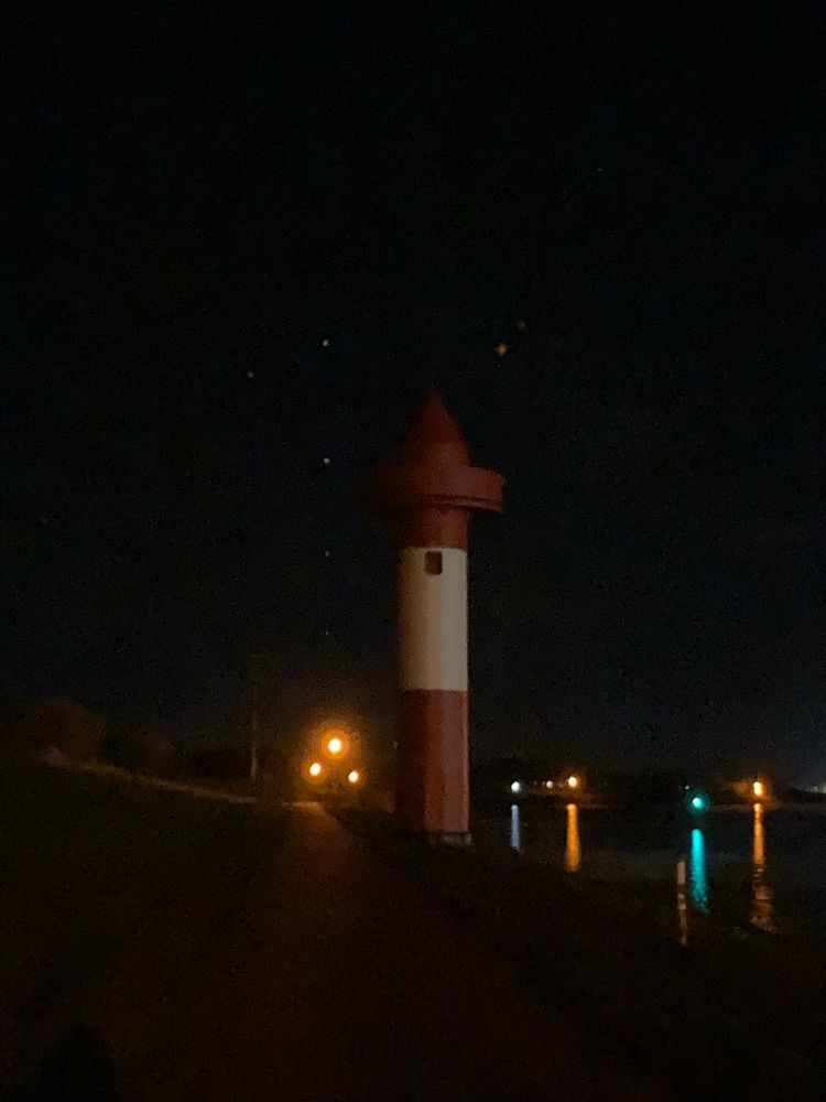 Ein Leuchtturm im dunklen, Sterne und Starlink am Himmel.