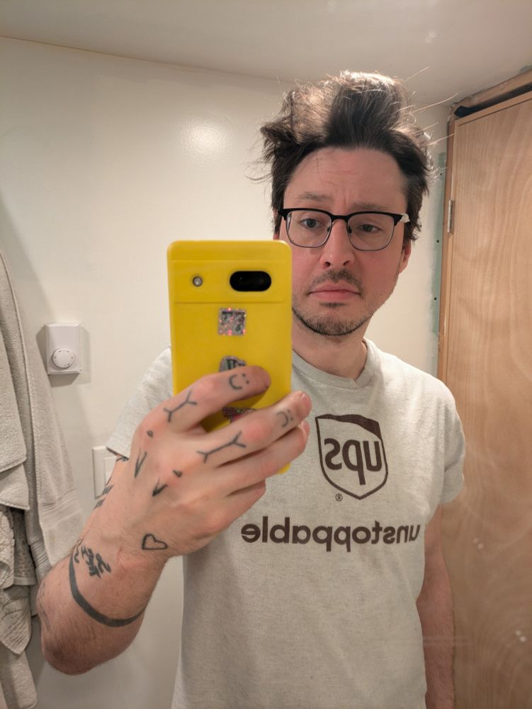 A confused looking man with unkempt hair taking a selfie 