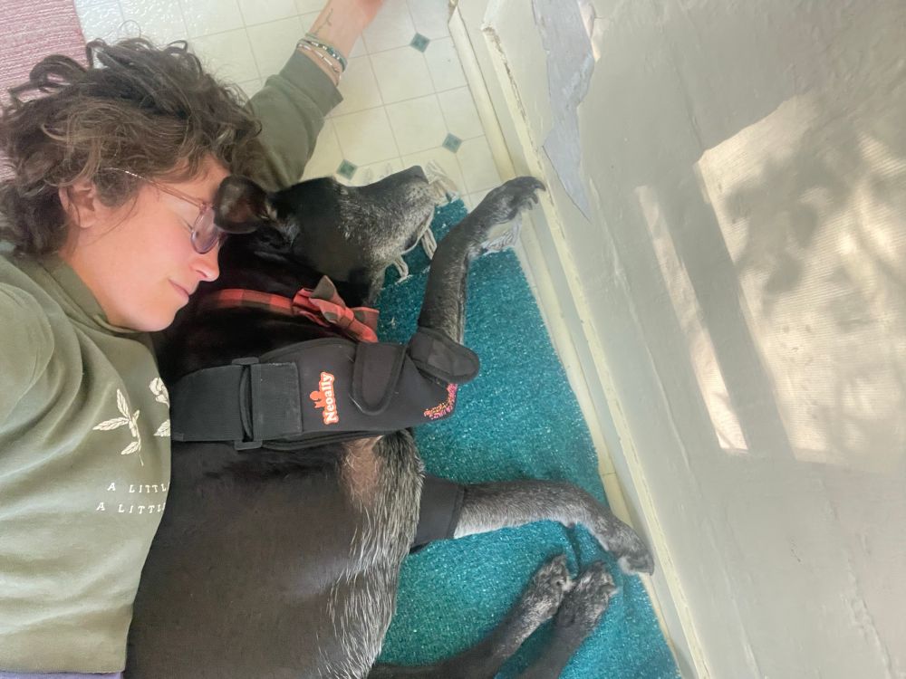 Andy and their dog Porter lie spooning. Andy forehead touches the back of Porter’s head. 