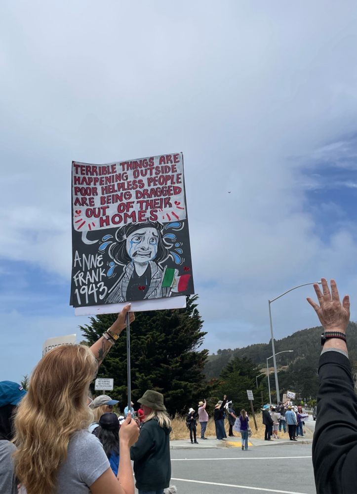 photo of a hand-painted sign with a Mexican flag and an image of Anne Frank saying “terrible things are happening outside, poor helpless people are being dragged out of their homes”