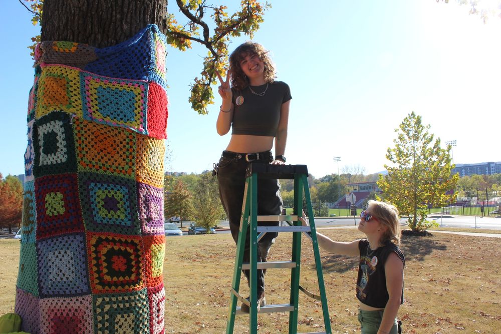 two students with Zero Hour Arkansas next to a tree wrapped in crocheted squares