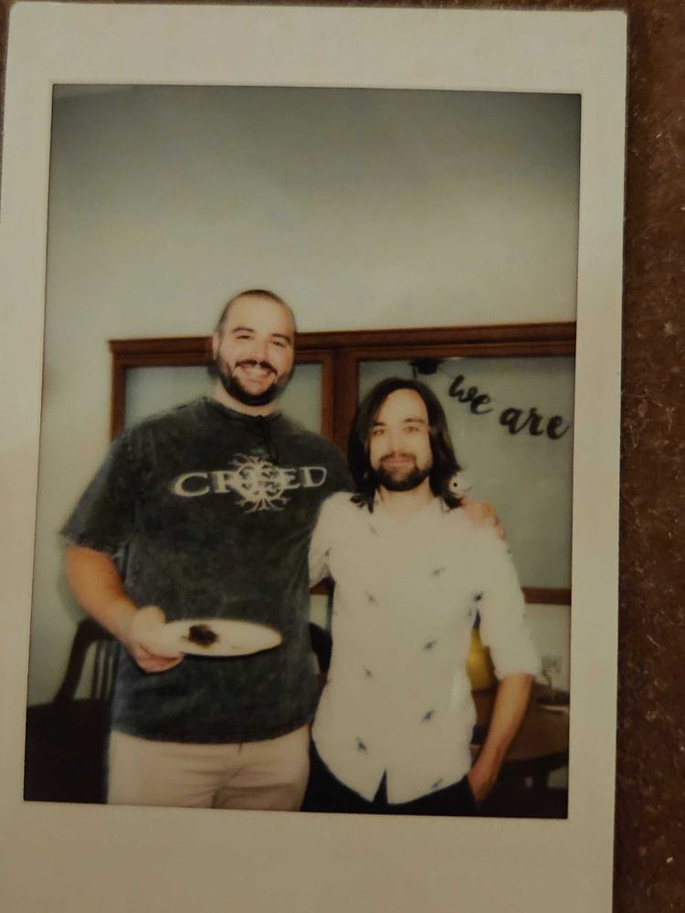 Two men standing together. One is wearing a creed shirt.