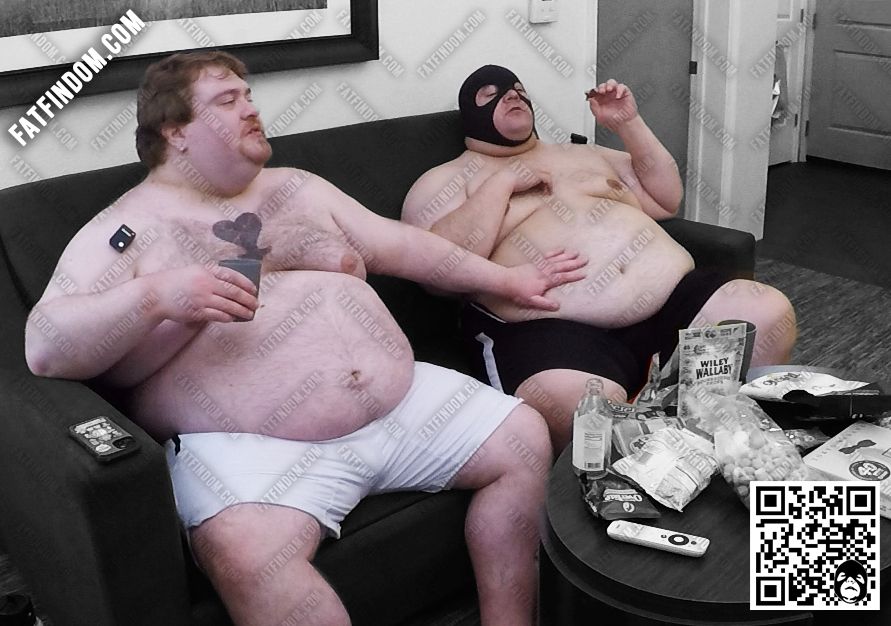 Two obese shirltess men sitting on a loveseat. One is in a black mask eating a Reese's Peanut Butter Cup while the other man holds a glass with one hand while the other touches the masked man's belly. The image is branded with FATFINDOM.COM in one corner and a QR code in the bottom right that leads to https://fatfindom.com