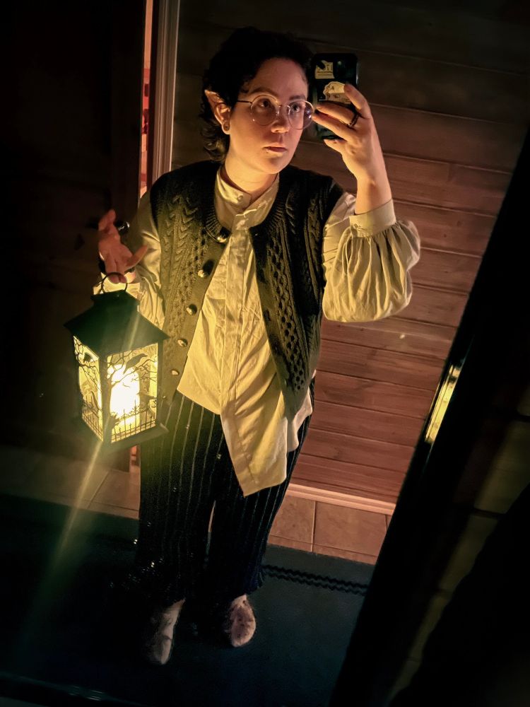 a mirror-selfie of yours truly holding a lit lantern,  dressed as a hobbit; pointy ears, a puffy-sleeved dress-shirt, green knit vest, striped linen capris, knitted socks made to look like bare feet with huge tufts of hair on top