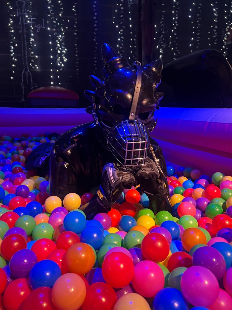 Photo of a latex dragon laying in a ballpit, resting his head on his hands