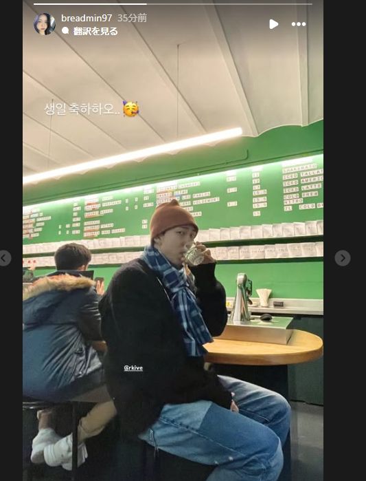 ニット帽をかぶってマフラーを巻いたナムがカメラ目線で、何かを飲んでいる。