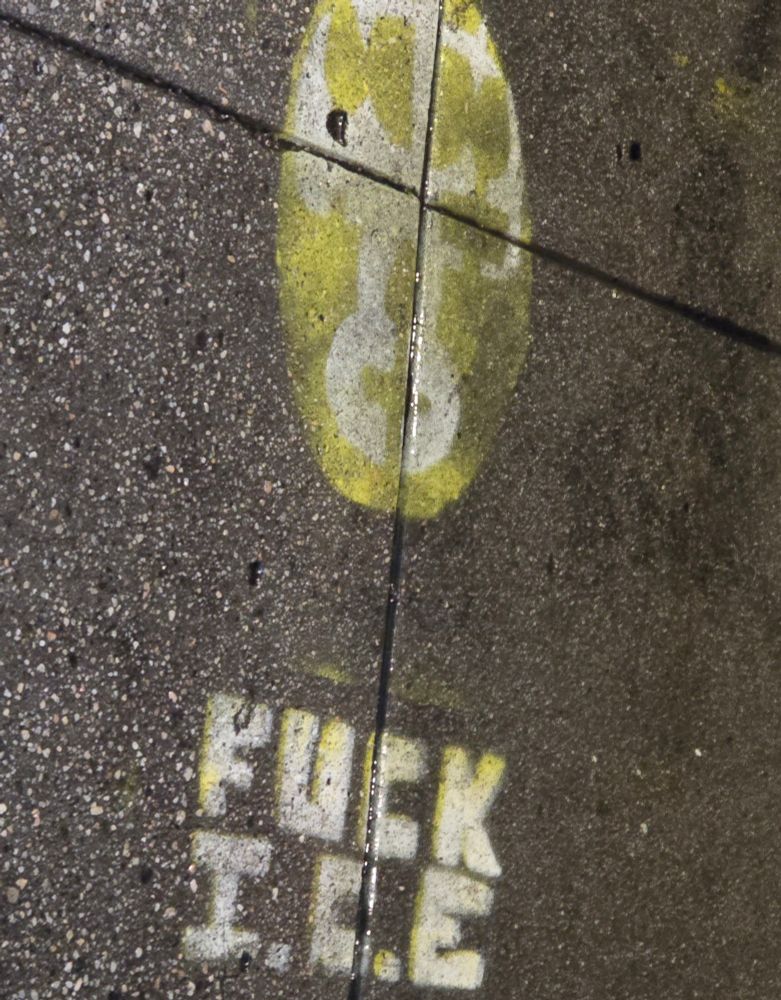 sidewalk graffiti  of a yellow luchador mask with the text "fuck i.c.e."  beneath 