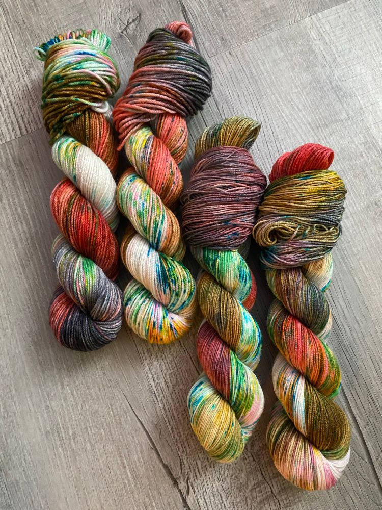 Four skeins of wound multicolored yarn are arranged on a grey background