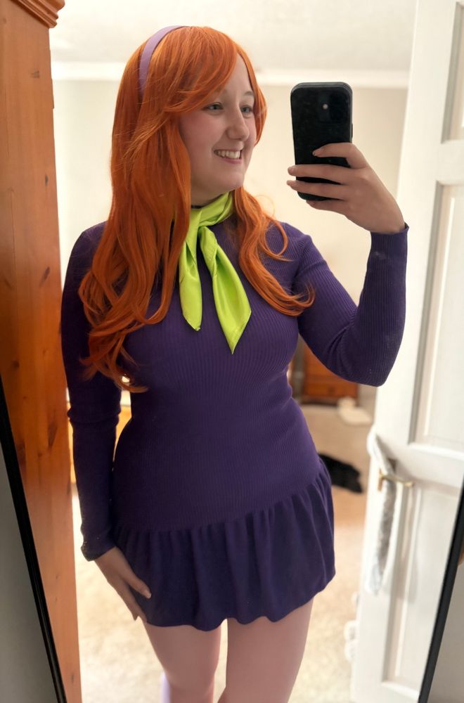 Photo of me dressed as Daphne wearing a purple dress, pink tights, red wig, and a green necktie.