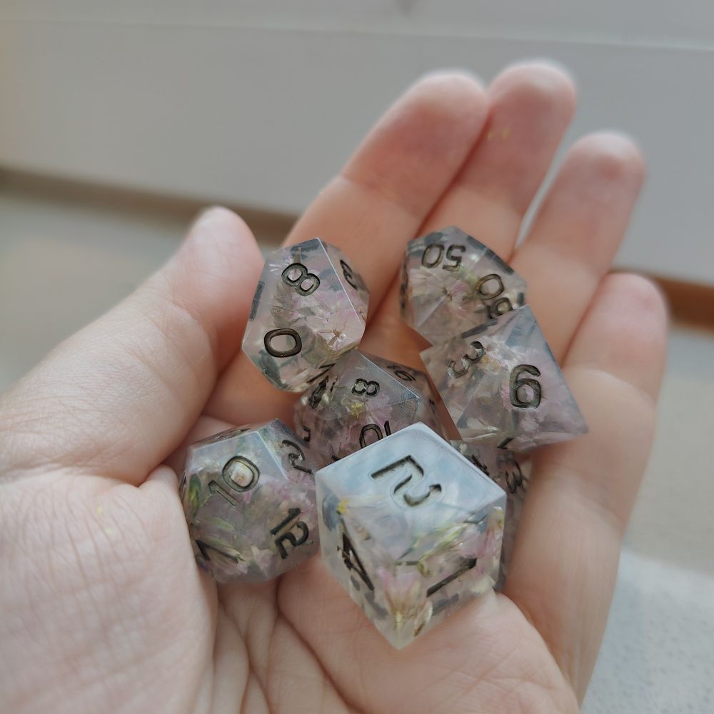 A 7 piece polyhedral set with bronze ink and pink flowers. They are being held in a hand.