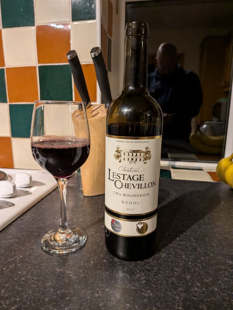 A glass of red wine and the bottle it came from on a kitchen surface.  The label reads "Chateau Lestage Chevillon Cru Bourgeois 2017".
