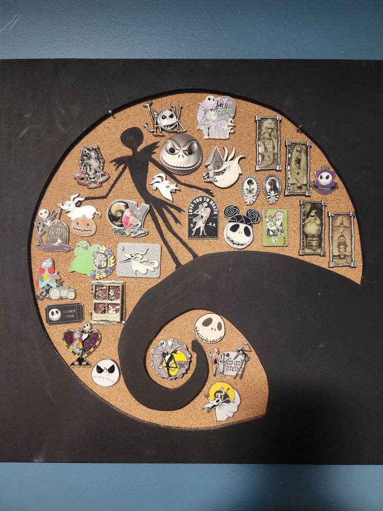 Cork board with a wooden frame including the iconic curly hill. Jack silhouette painted on it. 30 Nightmare Before Christmas pins on it. Some of them are the ones you've seen over the previois 30 days, some are not. This means that yes, I have more Jack and friends pins not pictured here and yes, I may have a pin collecting problem