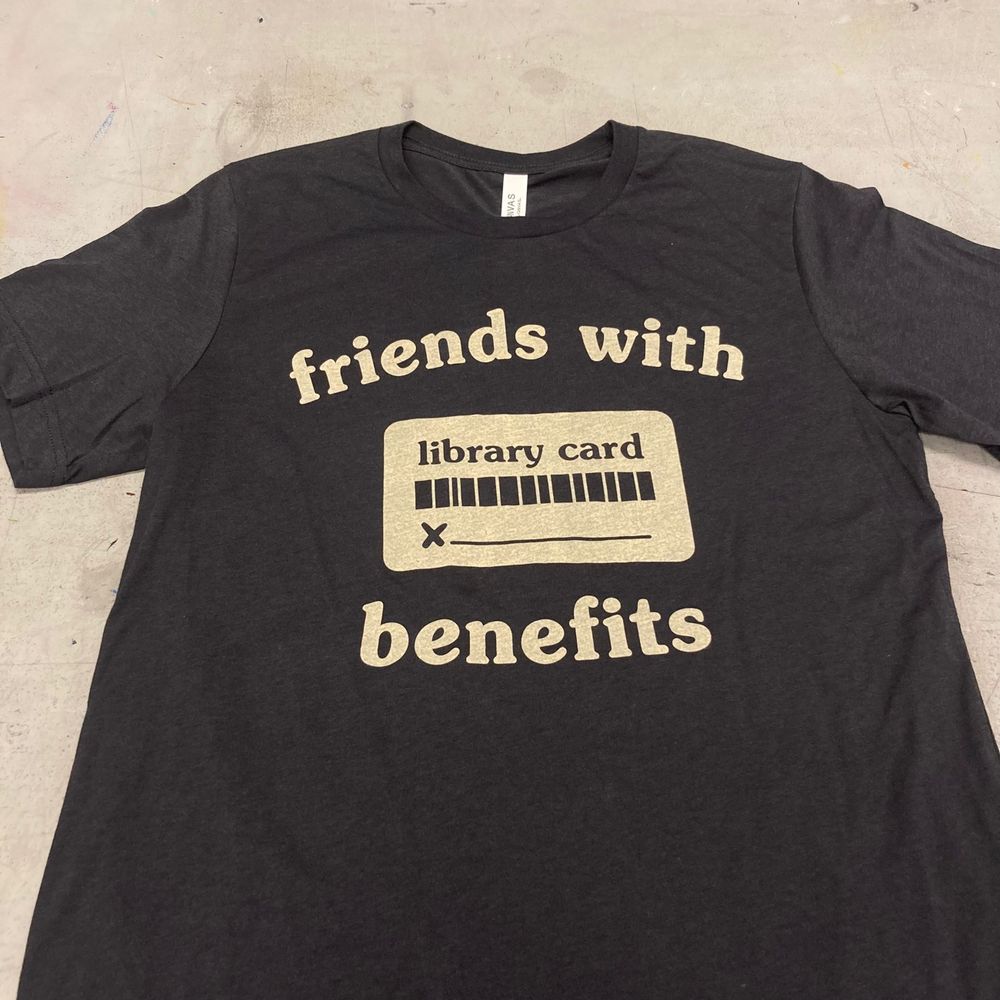a black t-shirt with white silk screened text that says "friends with benefits" surrounding a square box with barcode and signature line and the text "library card"