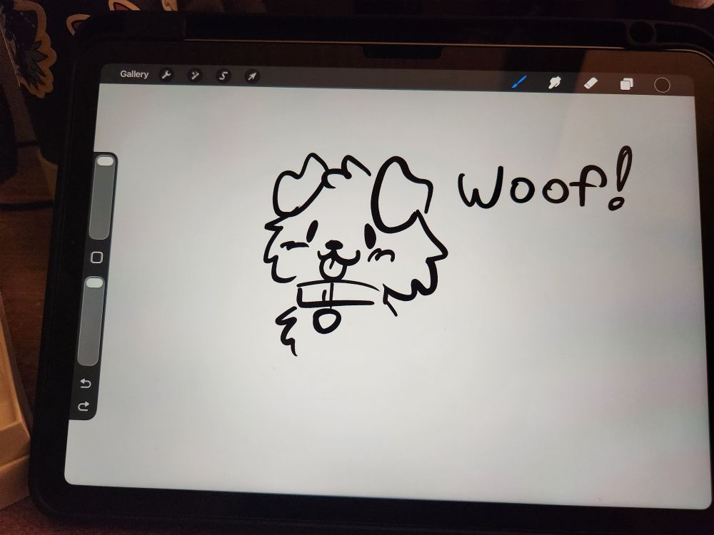 a picture of an ipad air sitting on a desk with procreate open, and a simple doodle of a puppy and the word woof drawn on the screen