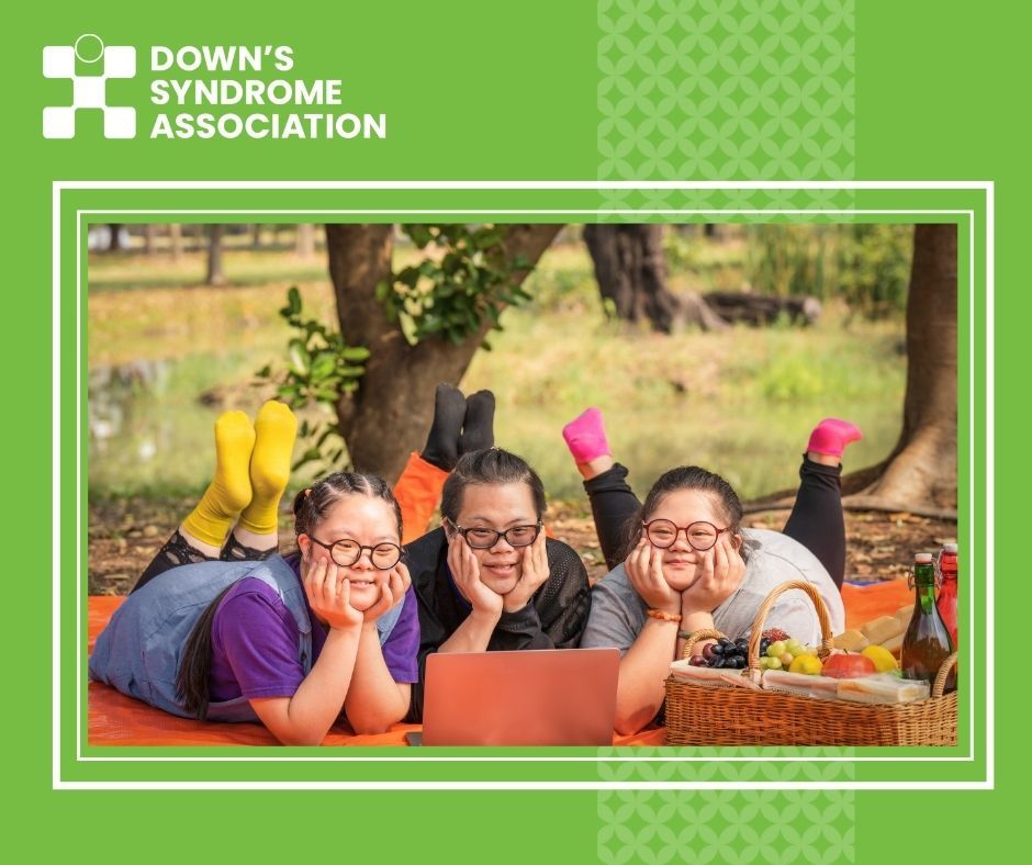 2 young women and one young man, all who have Down's syndrome, are pictured laying down with a picnic and with laptop.