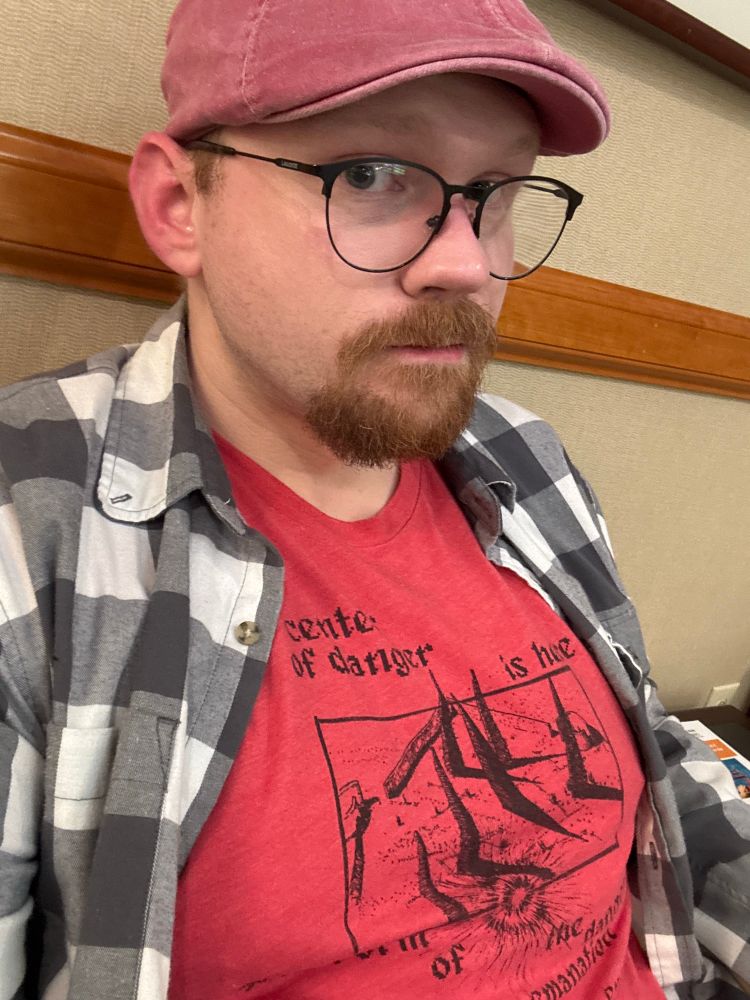 Our Hero, wearing a red cap and red tshirt with the text “the center of danger is here in the form of an emanation of energy” on it