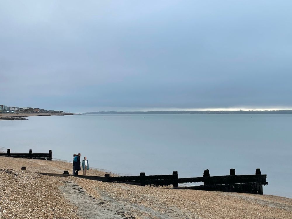 A stony beach in the foreground with a calm blue grey sea and sky merging together beyond 
