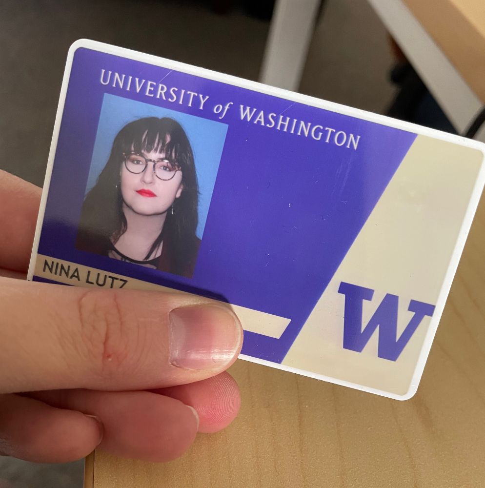 A University of Washington ID card that says "Nina Lutz" with Nina (dark brown hair, glasses, red lipstick) on the card.