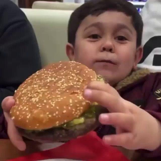 a young boy eating a hamburger with sesame seeds on the bun