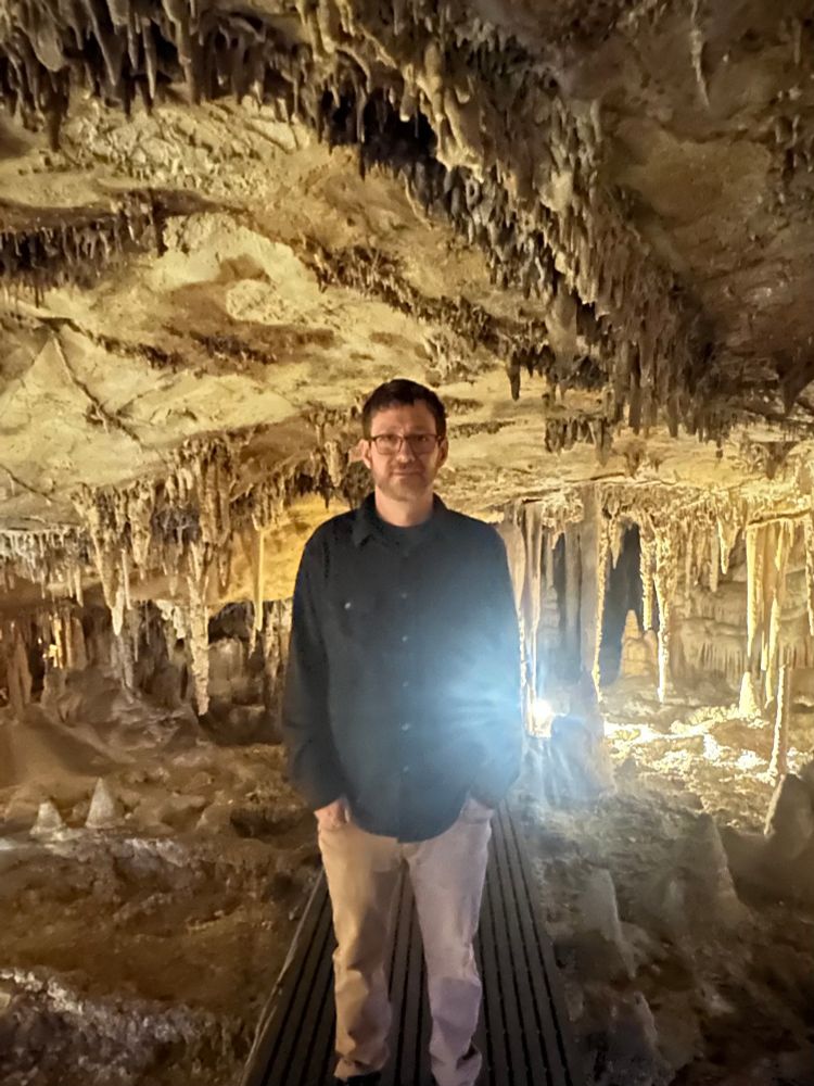 Old man with hands in pocket, in front of shit lighting, in a cave. 