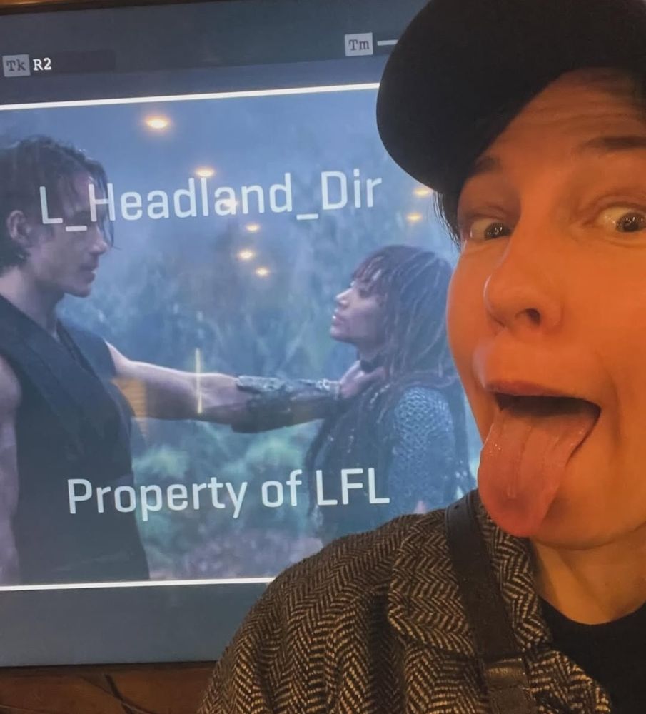 Rebecca Henderson in front of a bts still of the Qimir/Mae choking scene, with her tongue out
