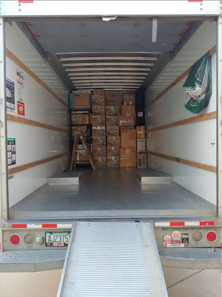 The truck less than half full. Shelving on the left with a step ladder in front of it. Girl_DM_ nui on center box top.