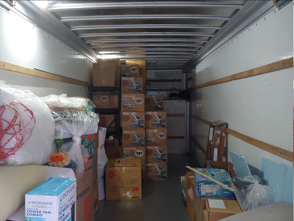 Girl_DM_ nui on a box in the center. Metal shelving unit in the back left. Boxes fill the shelves and in front of it. The attic section is not full yet, but have a path to the right for adding some. Some other packing material around.