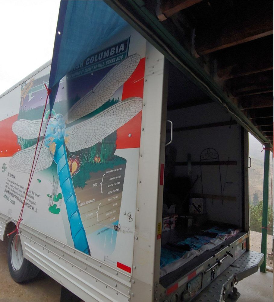 Back corner of the uhaul truck showing the tarp coming from the top deck area and tying down to the tire rim. Towels are in the truck door strip, to catch any that might make its way in, and allows us to dry our shoes off before going further in.