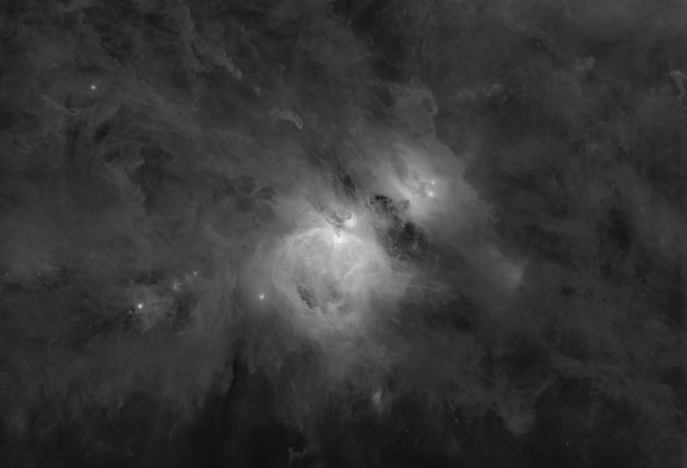 A monochrome image of the Orion Nebula and the dust and HII regions around it, forming extremely complex patterns caused by a cycle of star births