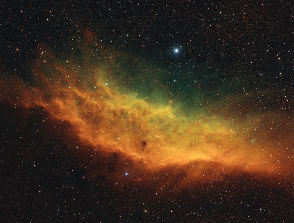 A space nebula that looks a bit like an ocean wave, in a color palette emphasizing various gas emissions, notably red and orange hues for hgydrogen and green and yellow hues for areas richer in sulphur and oxygen.