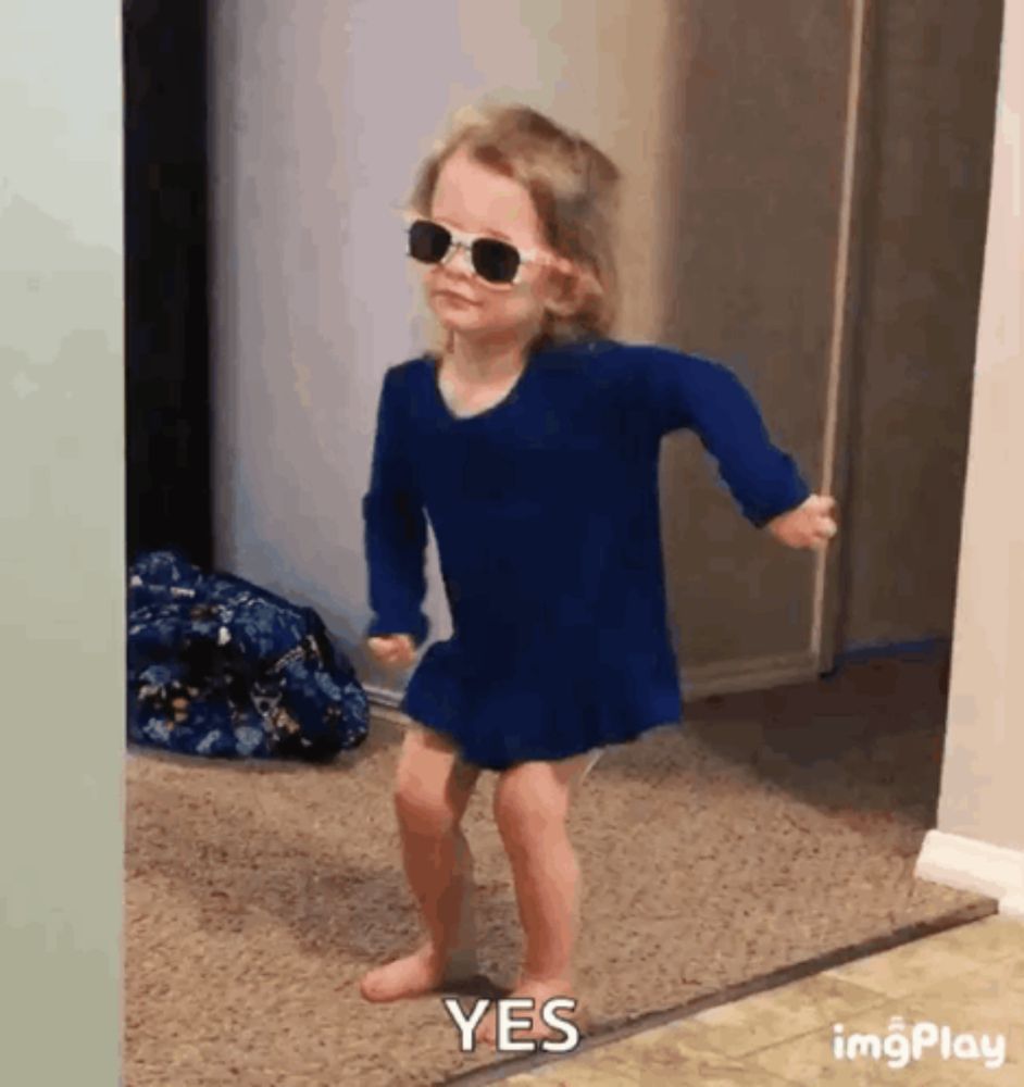 a little girl wearing sunglasses and a blue dress is dancing in a hallway .