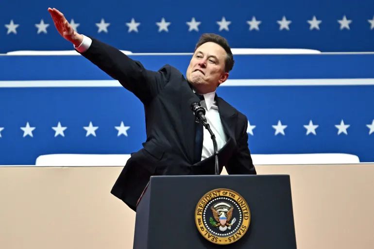 Elon Musk doing a full Nazi salute. He is standing behind the iconic blue lectern of the President of the United States. 