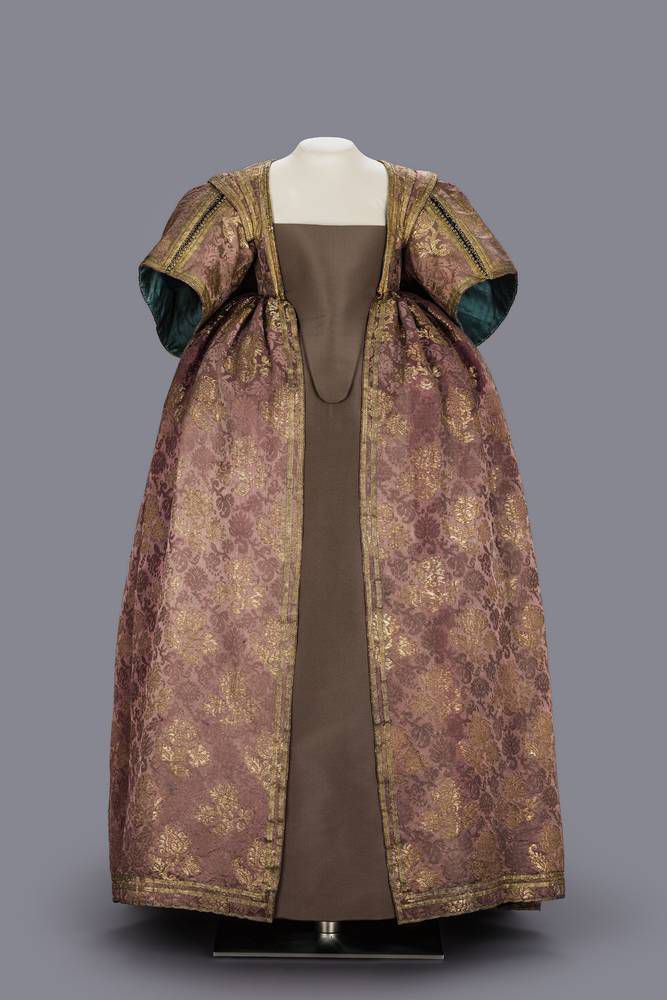 The women's outer garment is made of a magnificent gold-brocaded violet silk damask, the pattern of which, with large and small flower branches arranged in a diamond shape, is borrowed from Persian silk. Gold braids and gold trimmings emphasize the style of the dress, which dates back to the 1630s. In terms of its size and quality, the dress belonged to a small, girlish person of princely status. The dress, which was open at the front, formed the top part of a full-length women's dress. It consists of a bodice that ends below the breast and a wide skirt with folds. The outer garment was worn over a wide skirt that was lavishly decorated at the front. The breast was covered by a triangular bib with a protruding sash. The bib was laced on at the side, either hidden or visibly crossed. The half-length, wide sleeves of the outer garment encircle the elbow. The sleeve slit with many trimming buttons can be opened. The sleeve width is designed for the long, puffed sleeves that are pulled separately underneath. The dress was also worn with a shirt or shirt insert, lace collar and lace cuffs made of fine, white linen, colorful ribbon roses and precious jewelry. Electoral Princess Magdalena Sibylla of Saxony is considered to be the original owner of the dress. According to the one-sided back padding on the dress, the wearer suffered from a curvature of the spine. Evidence of such a disability can be found in various portraits of Magdalena Sibylla.