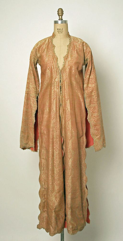 This garment is an Ottoman women’s robe, or entari, which would have been worn over a gömlek, or undershirt, and şalvar, or baggy trousers. The entari has a small stand-up collar, long straight sleeves open to the elbow, and long triangular pieces (peş in Turkish) added to each side of the front and back skirts for added fullness. Twelve buttons and loops at the bodice would have closed the garment. The skirt is open to the hip with pockets in the side seams above the slit. The fabric of the entari is a soft salmon-colored silk and cotton blend, with a gold pattern of undulating bands with floral bouquets between the bands, executed with extra weft metal-wrapped silk threads. The original lining of the garment is a coarsely woven fabric that has been treated with a heavy sizing or starch. At some point, the lower part of the garment and the sleeves were relined with a salmon twill, added on top of the original lining. The pocket lining is a striped floral savai, a silk brocade with alternating vertical bands of floral motifs composed of extra weft silk thread and a herringbone design executed in gold metal-wrapped thread. Most likely the lining was left over from another garment made in the same shop. All of the edges of the entari have been finished in a neat, scalloped design and narrow gold-wrapped braid, with extra loops and flourishes at the bodice and sleeve edges. The sleeve ends are further ornamented with an interlaced design carried out in a heavy gold thread.