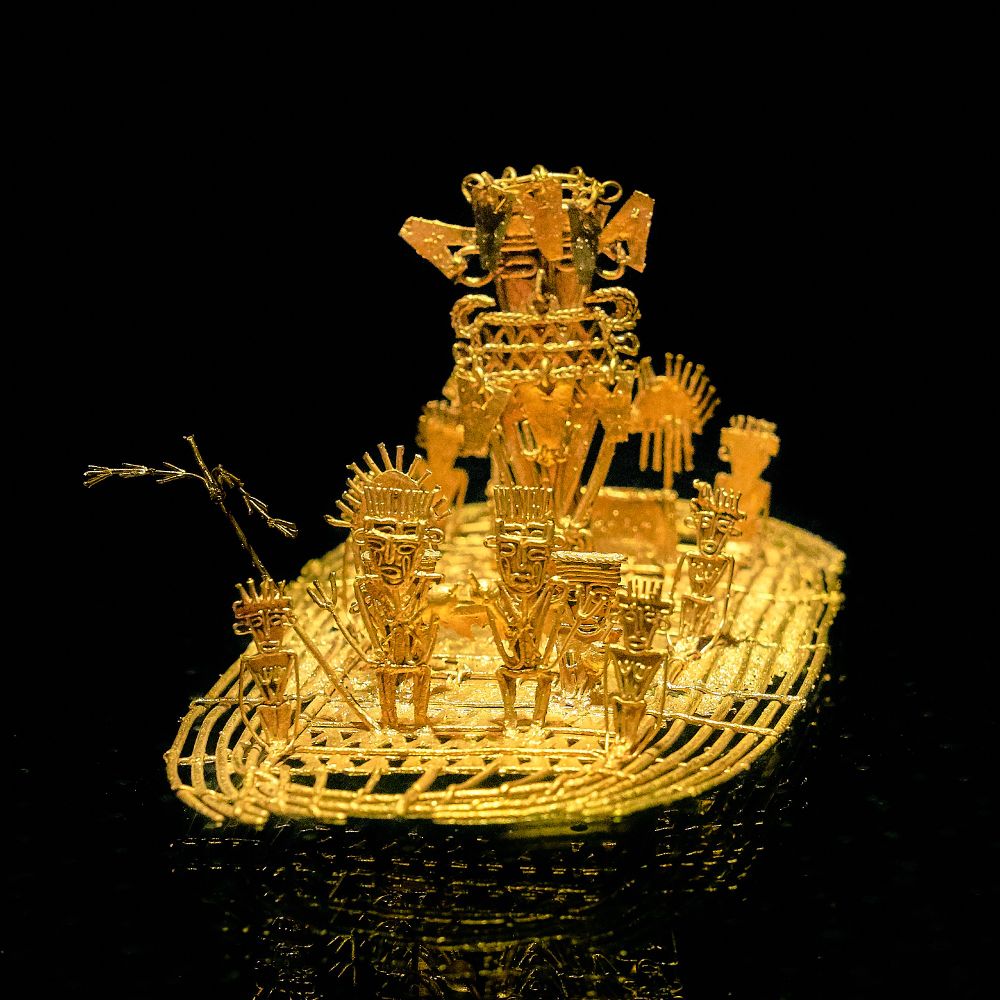 A golden raft with gold wire figures standing on it, elaborately dressed with headdresses, clothing, and staves. It is bright yellow gold against a black background.

By Pedro Szekely from Los Angeles, USA - Pedro Szekely, Gold Museum, Bogota, from flickr, CC BY-SA 2.0, https://commons.wikimedia.org/w/index.php?curid=74528973