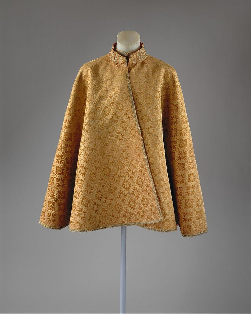 A gold cape with a high neck. The pattern has the typical reddish hue to it amidst the gold, and it would fall past someone's hands most likely. From the Met Museum.