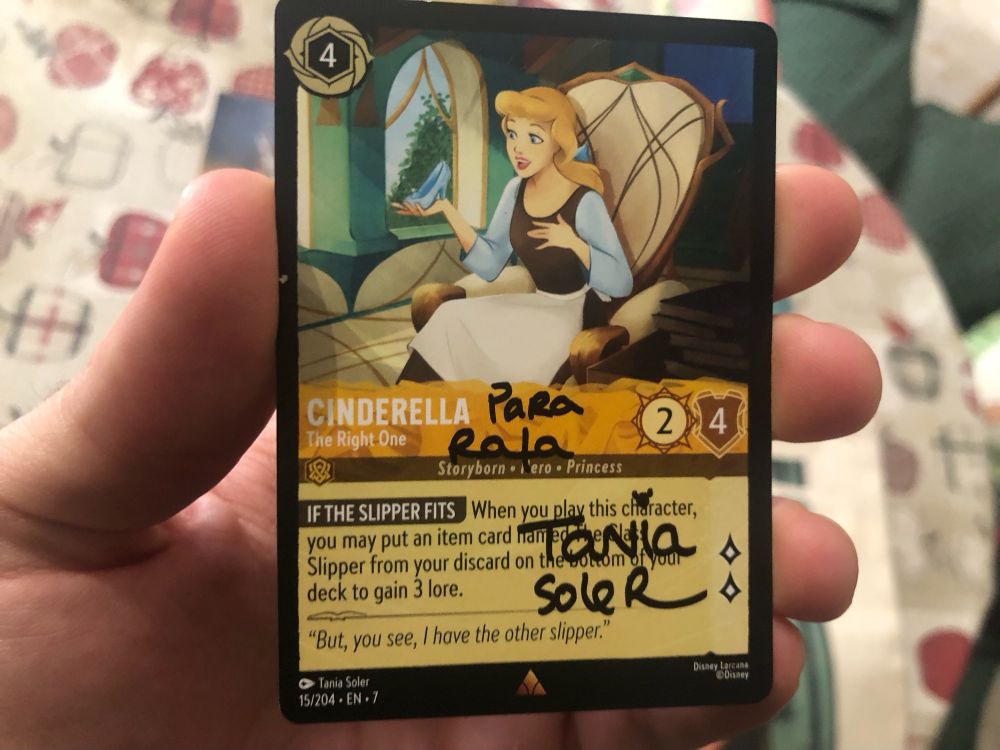 Carta del juego de cartas "Lorcana". Se ve a Cenicienta sosteniendo el zapato de cristal. Junto al texto de la carta, una dedicatoria que reza: Para Rafa; Tania Soler.