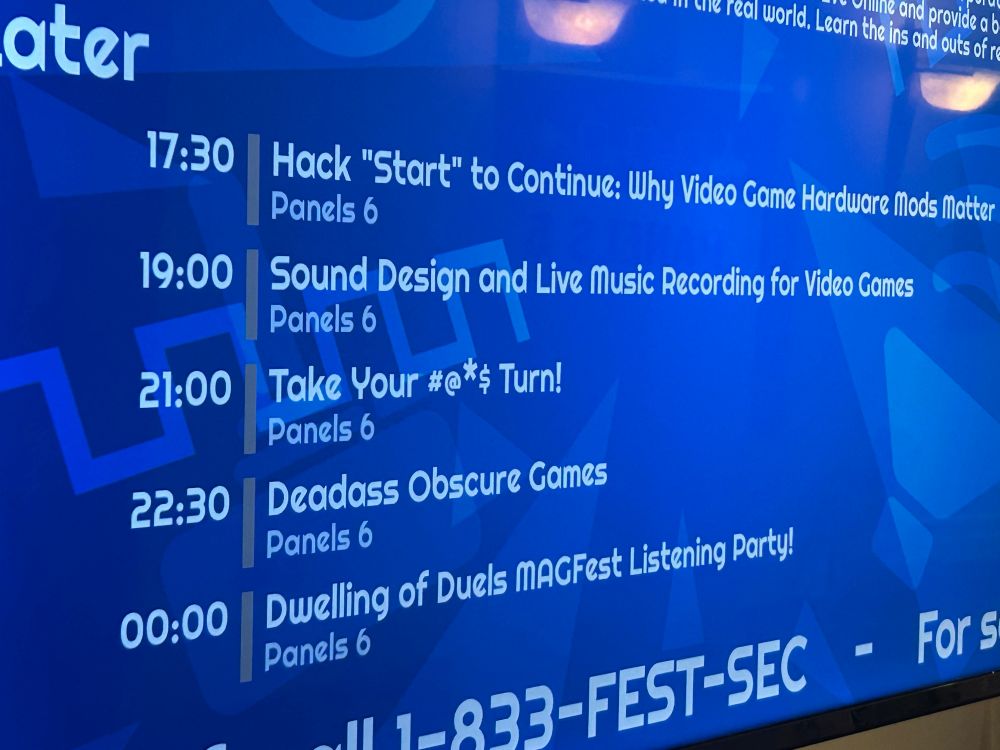A photo of a display at MAGFest noting the next set of panels in room Panels 6. My panel, Hack “Start” to Continue: Why Video Game Hardware Mods Matter, is at 5:30pm.