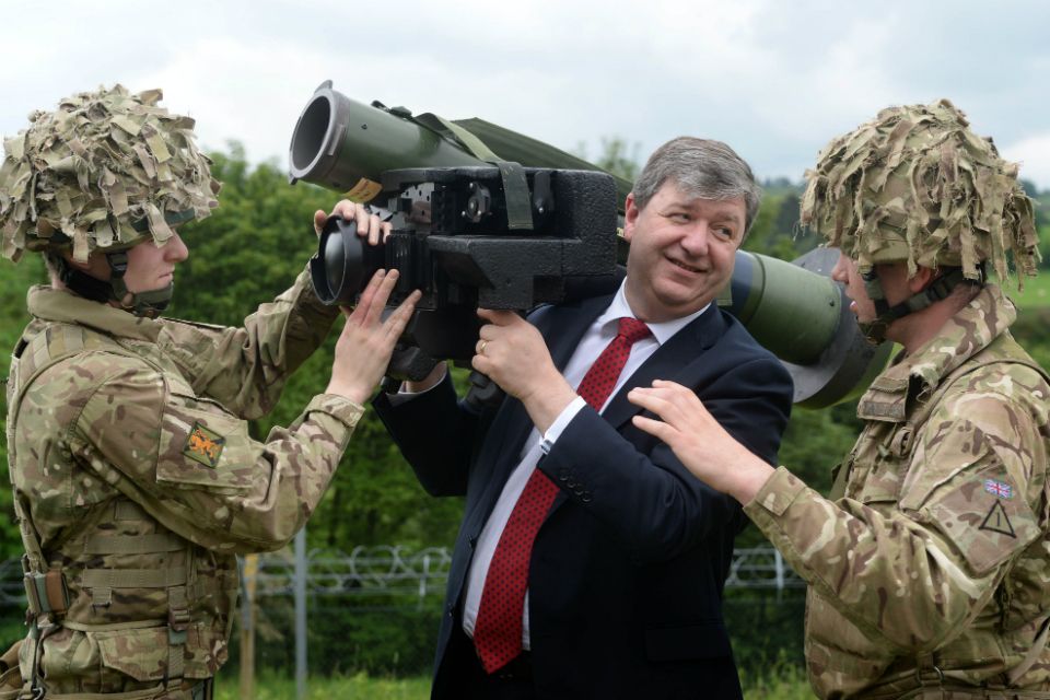 Alistair Carmichael holding a huge camera thing and being assisted by some soldiers.