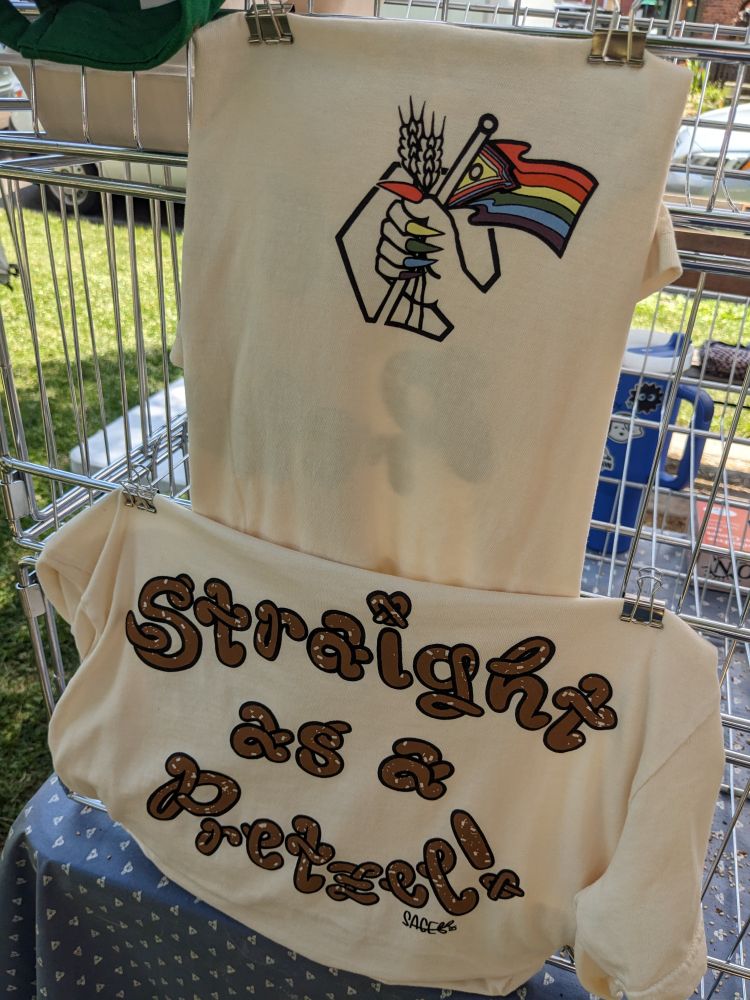 Shirt with a yassified BreadHive logo and pride progress flag on the front and "straight as a pretzel" in pretzel font on the back