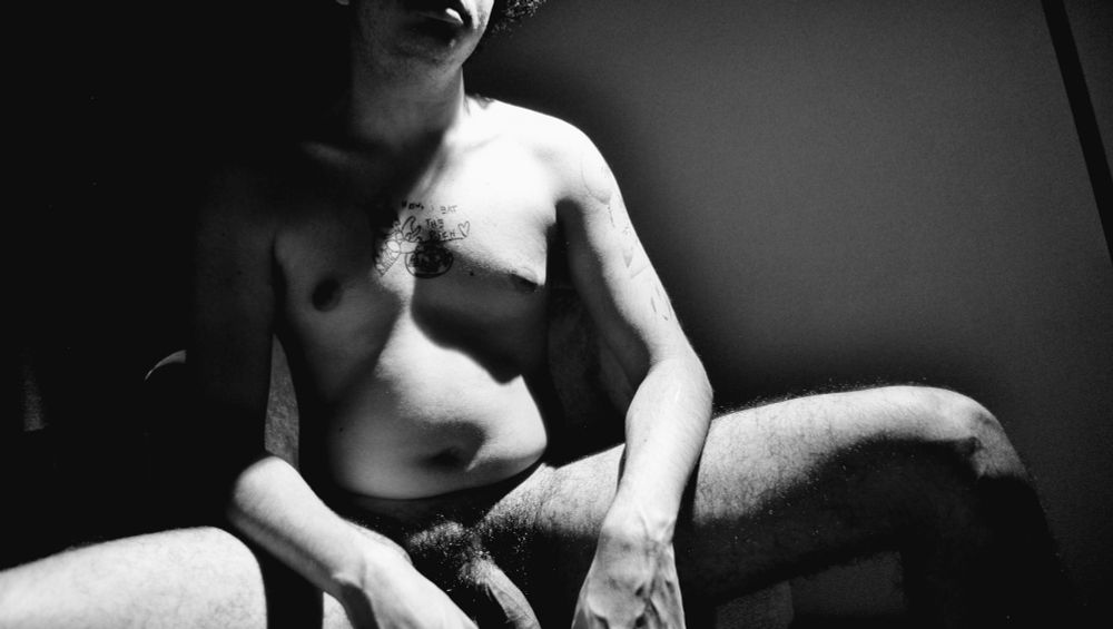 Nude de moi, en noir et blanc. Je suis assis, les jambes écartées, sexe apparent