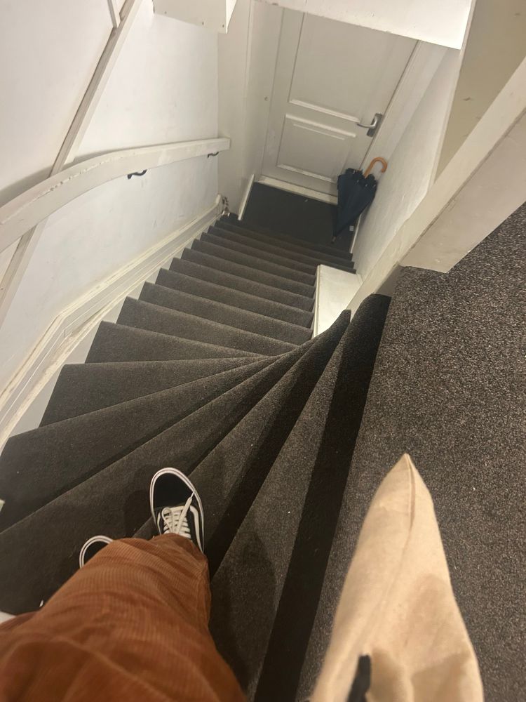 A foto mostra uma escada tipica holandesa. Ela tem uma primeira curva no começo, como em caracol e segue reta depois de 7 degraus.
A perna de uma pessoa vestida em calça marrom aparece no canto inferior esquerdo, com o pé não cabendo no degrau. Que em uma escada holandesa é minúsculo.