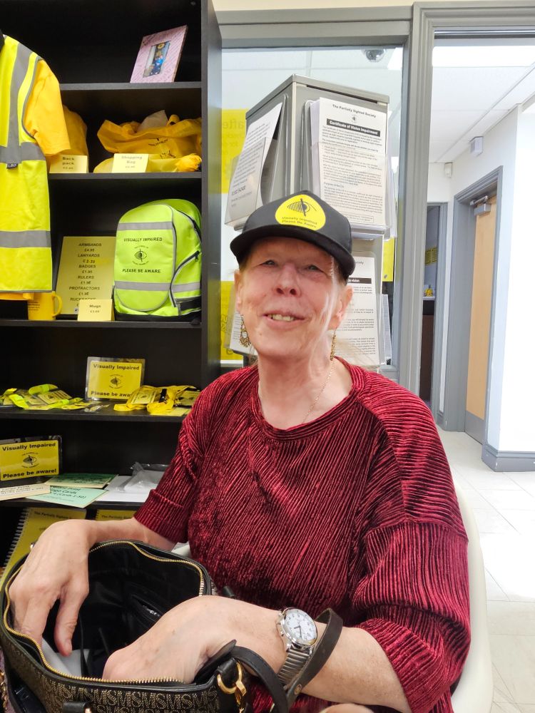 A woman wearing a black PSS branded baseball cap. The woman is smiling at the camera and has a red top on.