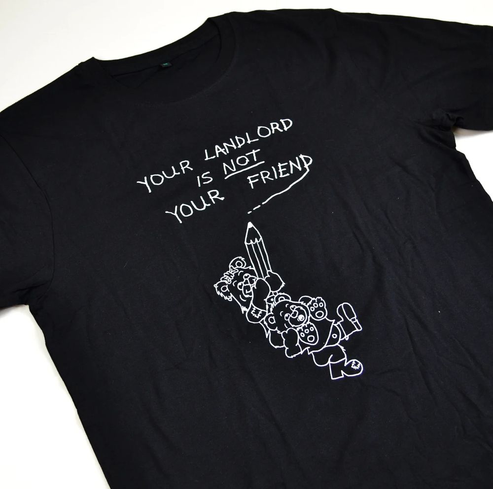 Picture of a black t-shirt with two teddy bears (one on the other's shoulders) holding a pencil having written the phrase 'Your Landlord Is Not Your Friend' 