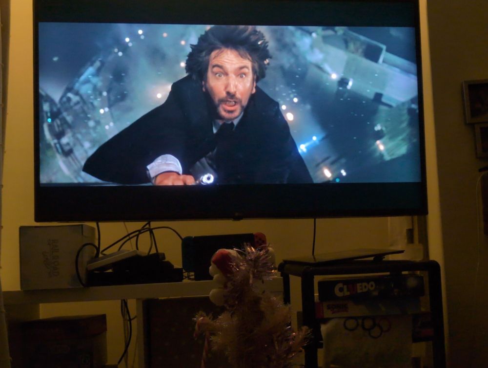 Hans Gruber falling on TV screen with small Christmas tree in foreground.
