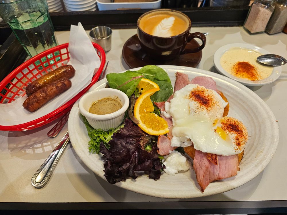 Diner style plate of eggs benedict, side of sausage links, and a small green salad.